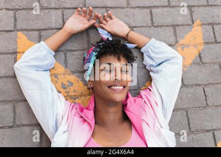 Carefree young woman with arms raised lying on road outdoors Stock Photo