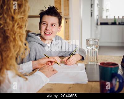 Son smiling while studying by mother at home Stock Photo