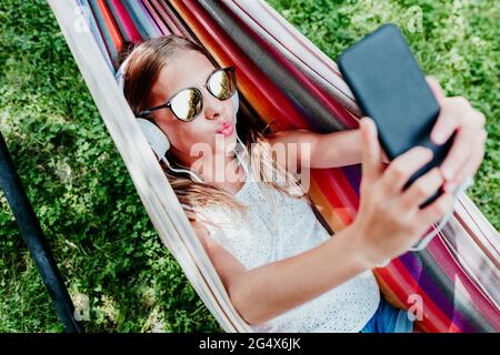 Girl wearing sunglasses puckering while taking selfie in hammock Stock Photo