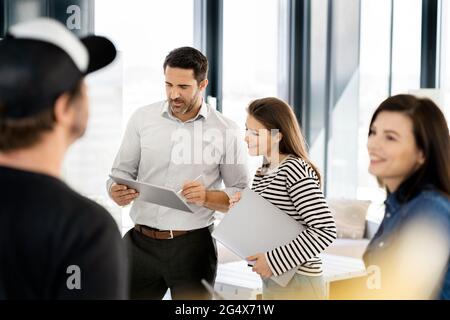 Male and female entrepreneur discussing over graphics tablet while colleagues discussing at office Stock Photo