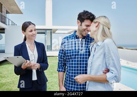 Female real estate agent smiling while standing by happy couple Stock Photo