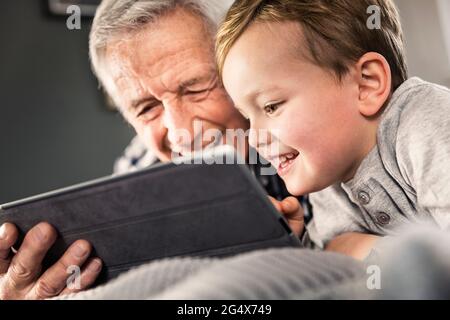 Smiling boy using digital tablet with senior man at home Stock Photo