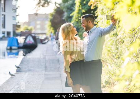 Happy couple looking at each other while taking selfie through smart phone Stock Photo