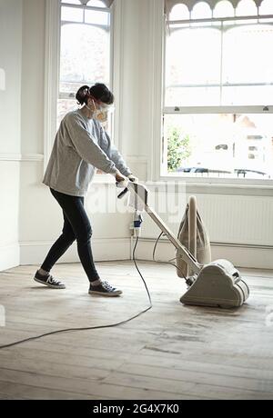 Woman sanding floorboards in empty living room Stock Photo