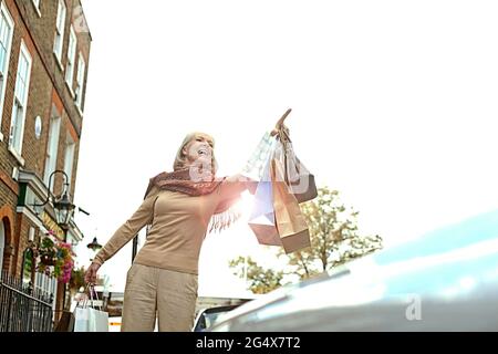 Smiling woman with shopping bags hailing taxi in city Stock Photo