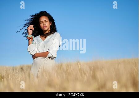 Beautiful woman with tousled hair standing in wheat field in front of blue sky Stock Photo