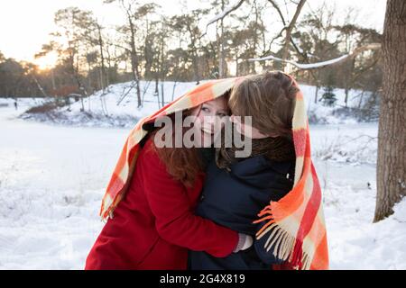 Cheerful young couple enjoying while wrapping in blanket during winter Stock Photo