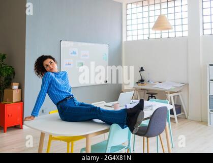 Thoughtful businesswoman sitting with legs crossed at ankle in office Stock Photo