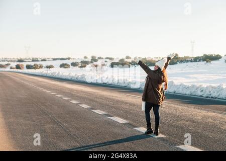 Carefree woman standing with arms raised on road during winter Stock Photo