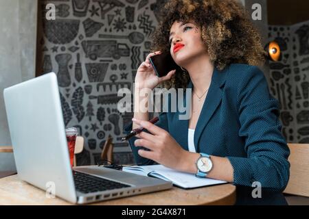 Female freelance worker talking on mobile phone at coffee shop Stock Photo