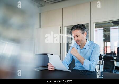 Male professional reading documents while sitting at desk in office Stock Photo