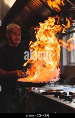 Chef with flame on frying pan in kitchen Stock Photo
