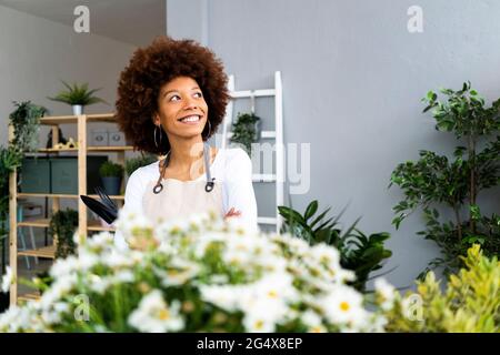 Thoughtful female shop owner smiling while looking away in plant shop Stock Photo