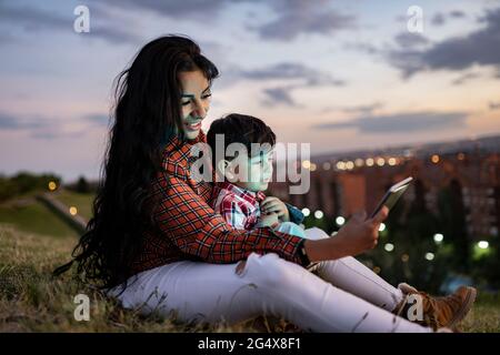 Mother using digital tablet while sitting with son on hill Stock Photo