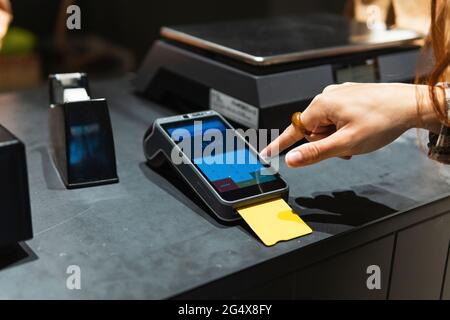 Female customer entering password on reader while paying through credit card at retail shop Stock Photo