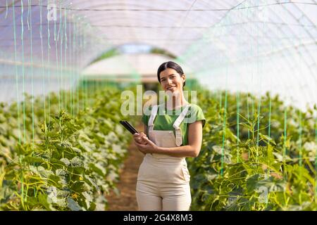 Confident female farmer holding digital tablet while standing at greenhouse Stock Photo