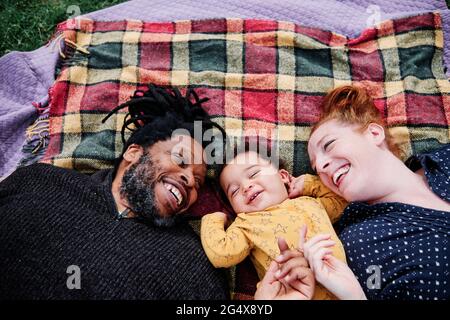 Happy family playing with cute son while lying on picnic blanket at park Stock Photo