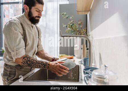 Bearded man washing bowl in kitchen Stock Photo