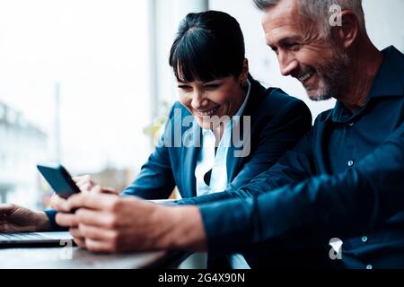 Smiling business couple using mobile phone at cafe Stock Photo