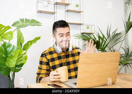 Smiling young male professional waving while doing video call through laptop in office Stock Photo