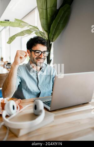 Happy young male freelancer with clenched fist using laptop at cafe Stock Photo