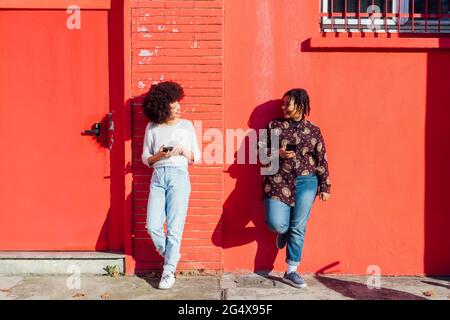 Multi-ethnic friends talking while leaning on red building Stock Photo