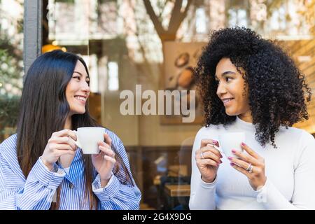 Smiling young woman looking at female friend while having coffee outside bar Stock Photo