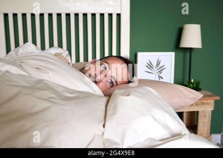Man contemplating while lying in bed at home Stock Photo