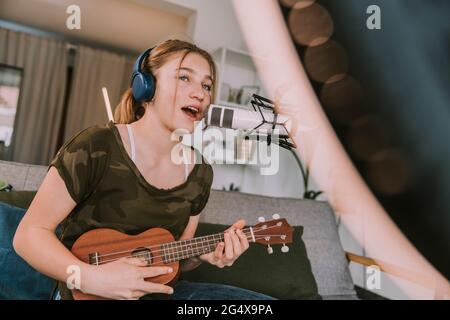 Female singer playing ukulele singing on microphone while vlogging at home