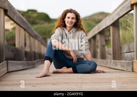 Young woman sitting on wooden bridge during vacations Stock Photo