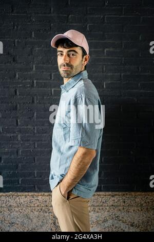 Young man with hand in pocket standing by wall Stock Photo