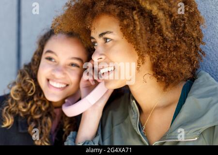 Female friends sharing headphones while listening music Stock Photo