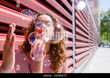 Playful young woman blowing bubbles on sunny day Stock Photo