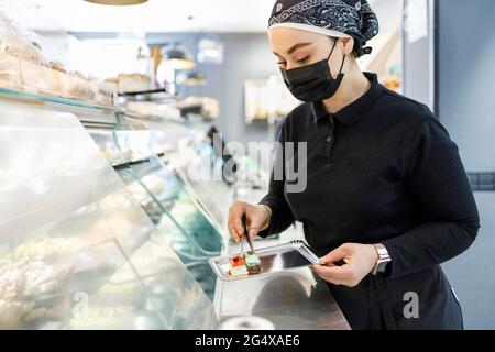 Female owner with cake on tray at display cabinet in bakery Stock Photo