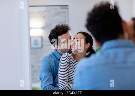 Boyfriend kissing girlfriend on cheek in front of mirror at home Stock Photo
