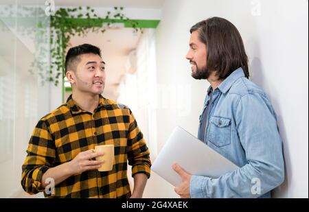 Male coworkers discussing together while standing in office Stock Photo