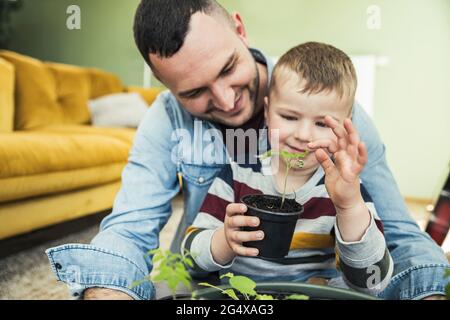 Smiling father sitting with son holding potted plants in living room Stock Photo