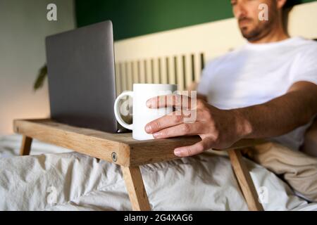 Man working on laptop while sitting in bed at home Stock Photo