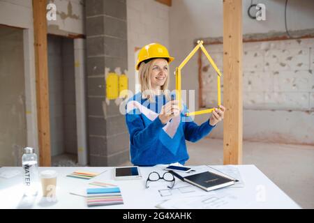 Smiling female building contractor making house shape with folding ruler at construction site Stock Photo