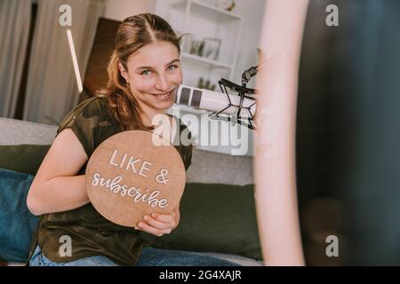 Smiling girl showing like and subscribe sign at home Stock Photo