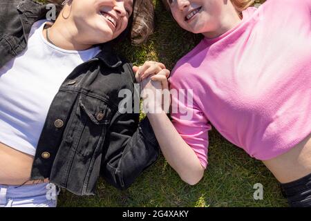 Happy female friends with holding hands lying on grass in public park Stock Photo