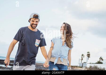 Smiling mid adult couple holding hands while walking at beach Stock Photo