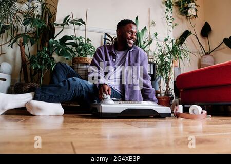 Smiling man sitting by turntable on floor at home Stock Photo