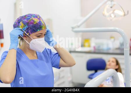 Female dentist removing protective face mask with patient in background at medical clinic Stock Photo