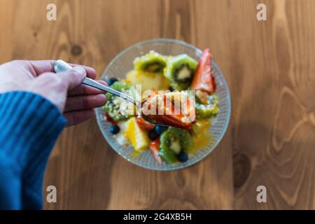 Man's hand holding spoon while eating fruit salad in restaurant Stock Photo