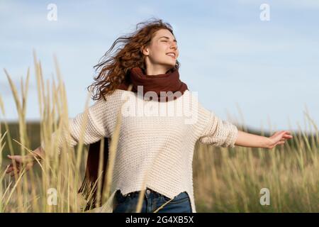 Young woman with arms outstretched smiling in dunes during vacations Stock Photo