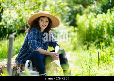 Smiling woman looking away while sitting on hay in garden Stock Photo