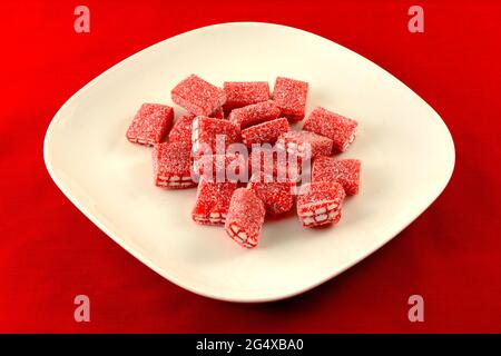 Strawberry gummy brick candy coated in sour sugar on white plate on red background Stock Photo