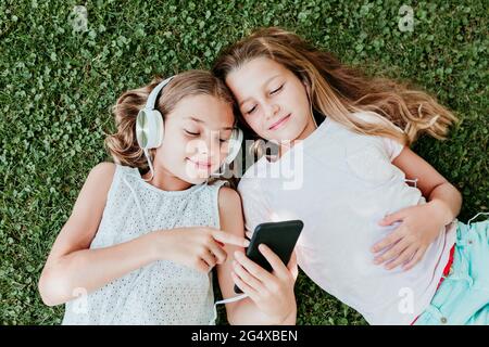 Smiling friends listening music while lying on grass in summer Stock Photo