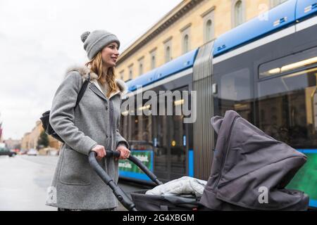 Smiling woman pushing baby stroller while walking in city Stock Photo